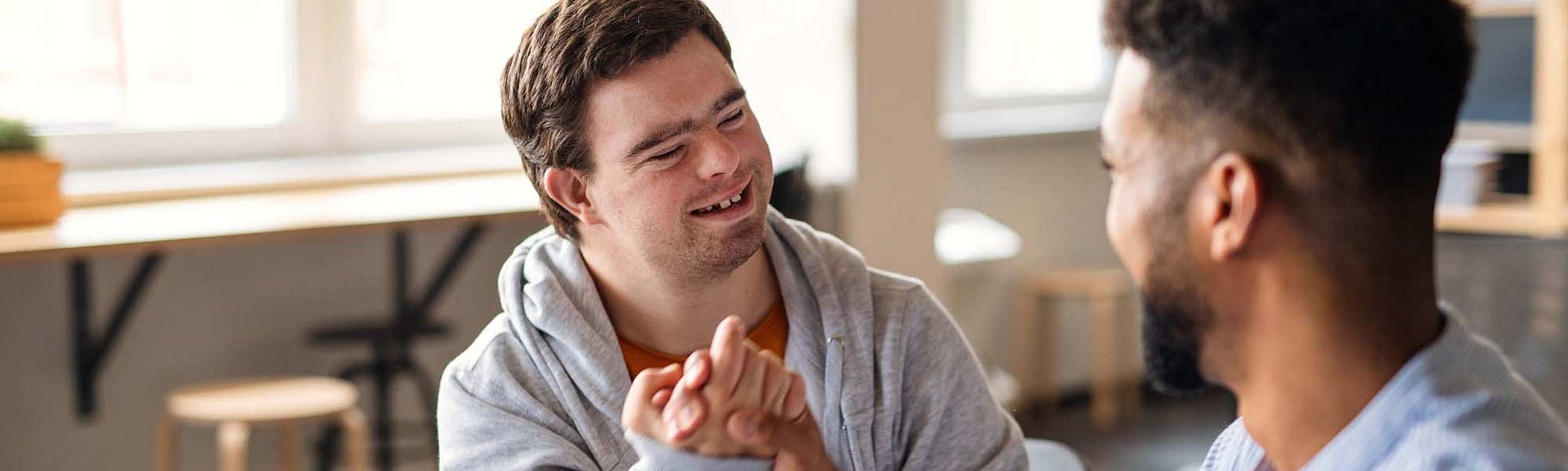 Zwei Personen im Gespräch. Eine ist nur von hinten zu sehen, eine hat das Down Syndrom. Sie geben sich die Hand.